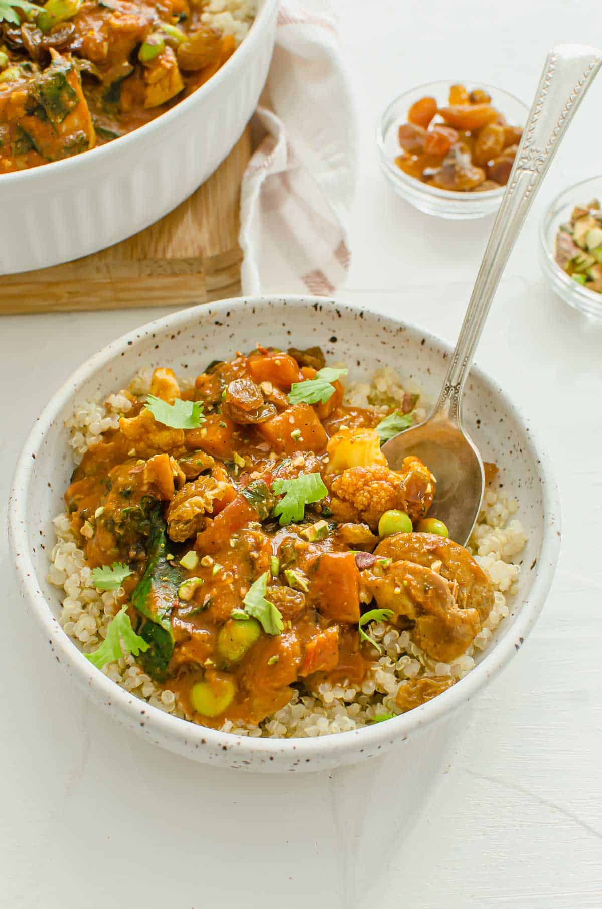 Chicken sweet potato curry in a bowl with a spoon inside with cilantro, pistachio, and golden raisins on top.