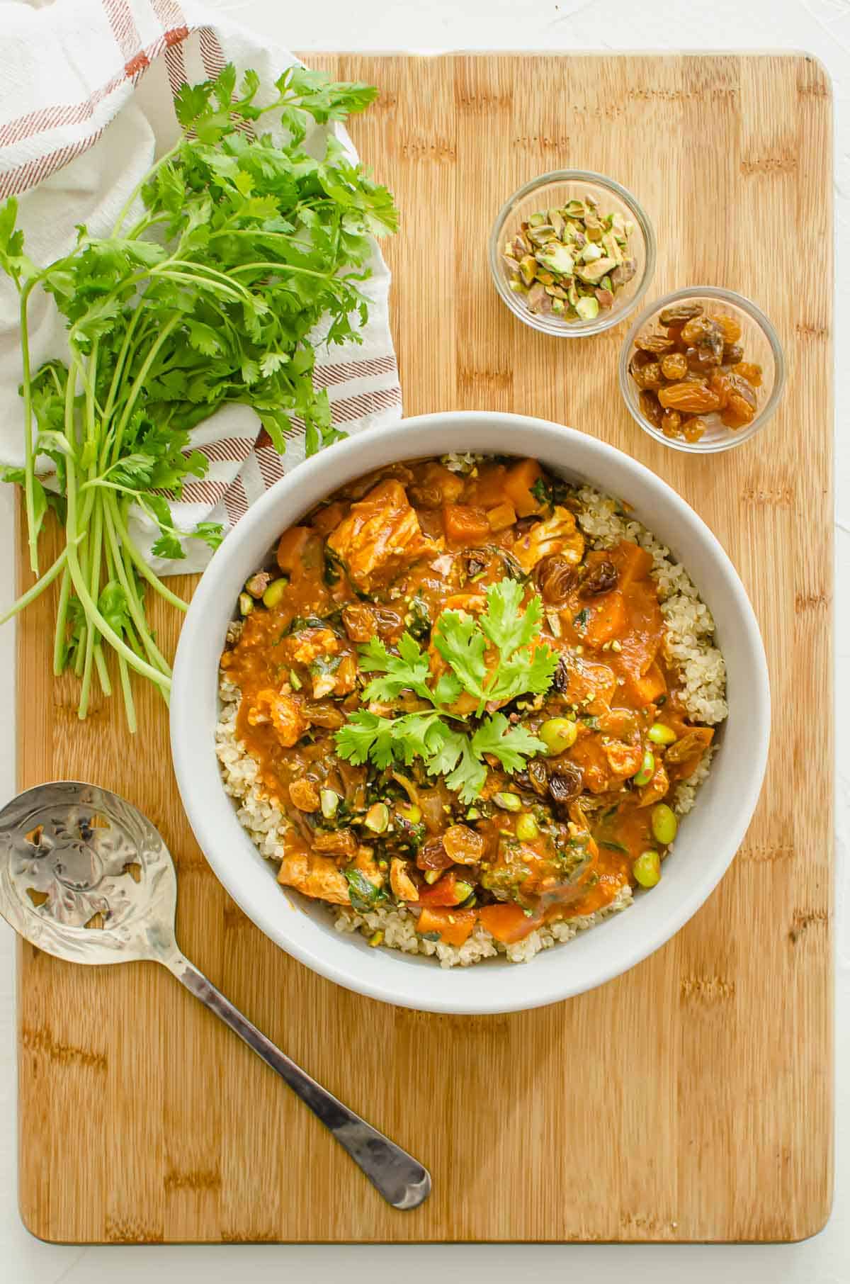 White bowl with chicken sweet potato curry served on quinoa on a wooden cutting board.