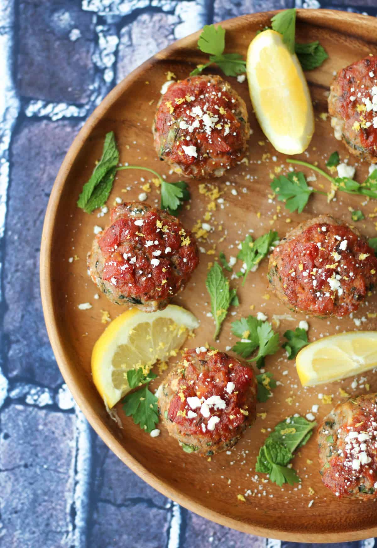 Birds eye view of savoury Greek balls on a wooden plate topped with feta and garnished with mint and lemon wedges.