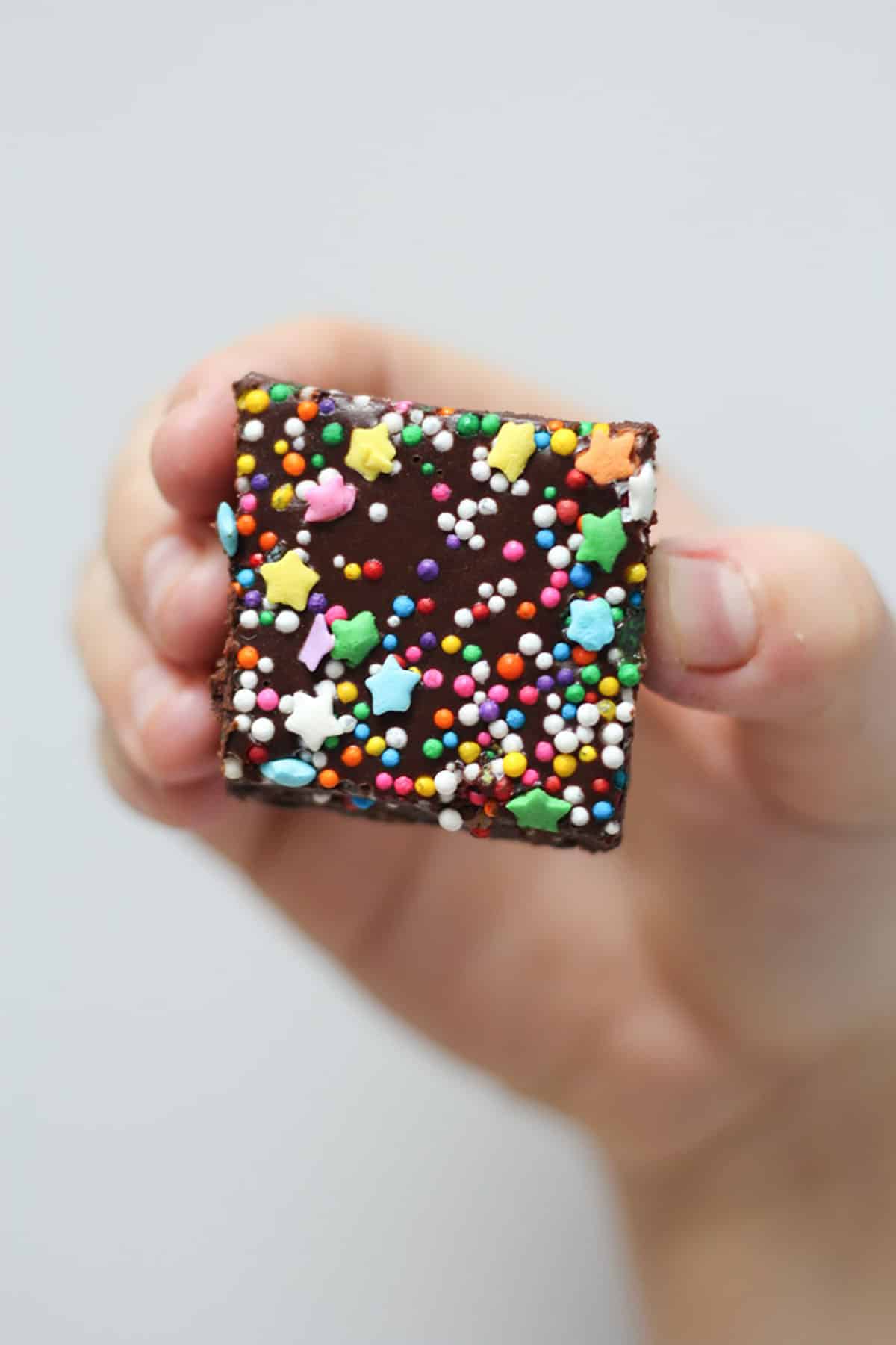 Hand holding up a no bake brownie square with rainbow sprinkles. 