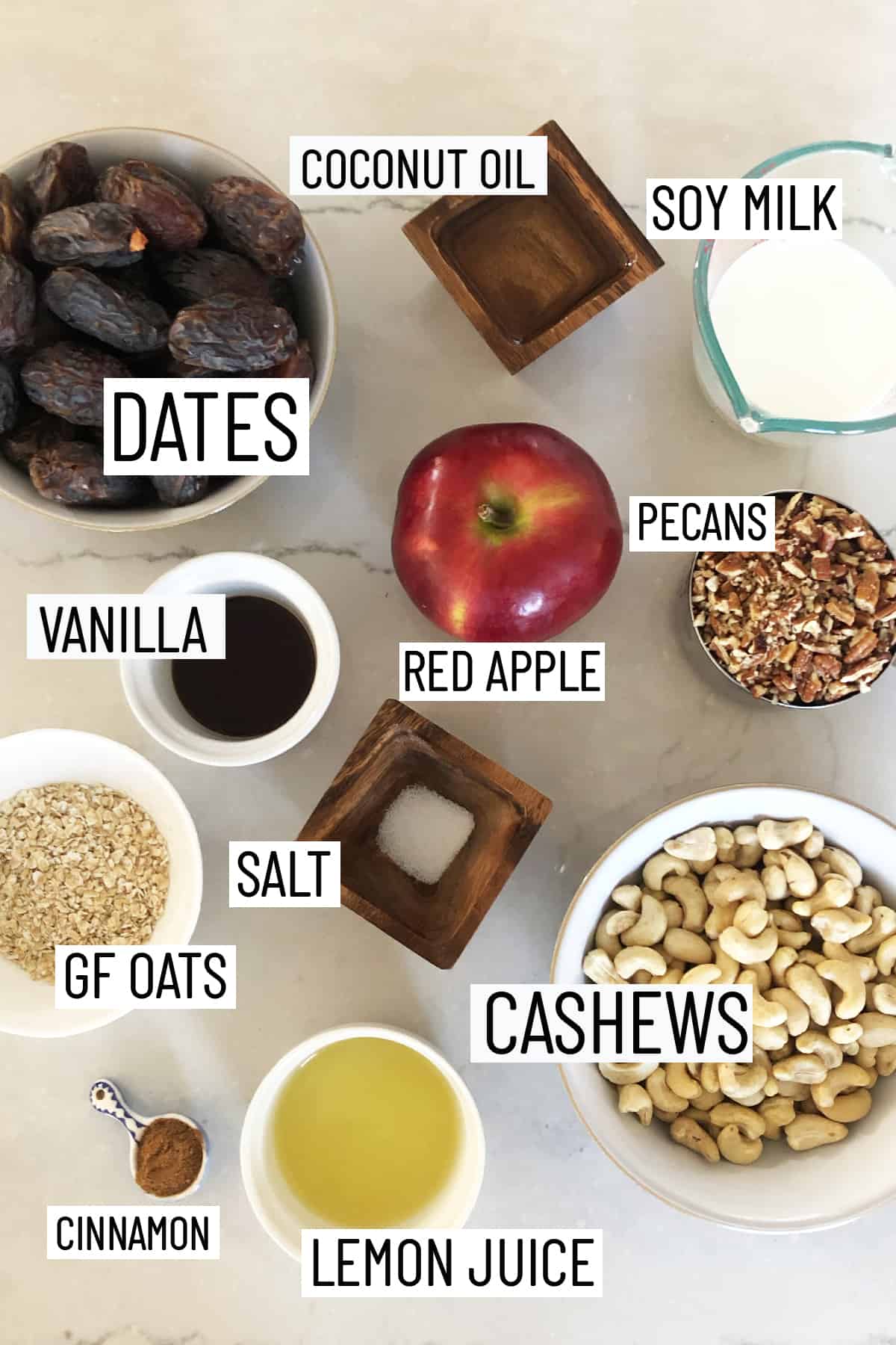 Flat lay image of portioned ingredients of raw vegan cheesecake including lemon juice, cinnamon, cashews, salt, oats, pecans, red apple, dates, vanilla, soy milk, and coconut oil. 