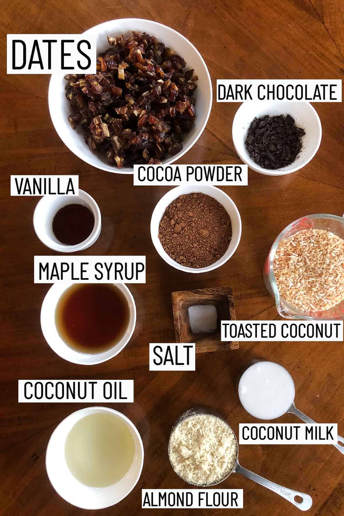 Flat lay of portioned recipe ingredients including almond flour, coconut milk, coconut oil, salt, maple syrup, toasted coconut, cacao powder, vanilla, chocolate, and dates. 