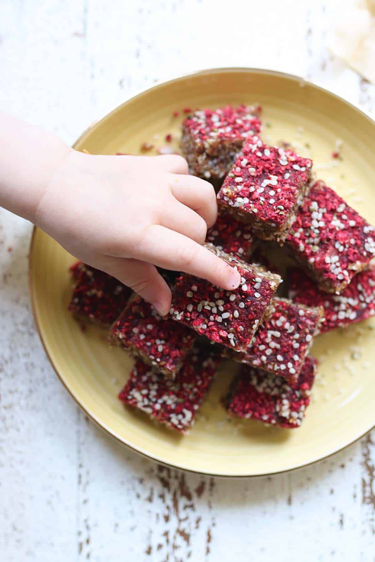 Birds eye view of granola bars on a yellow plate with a babies hand reaching for one. 