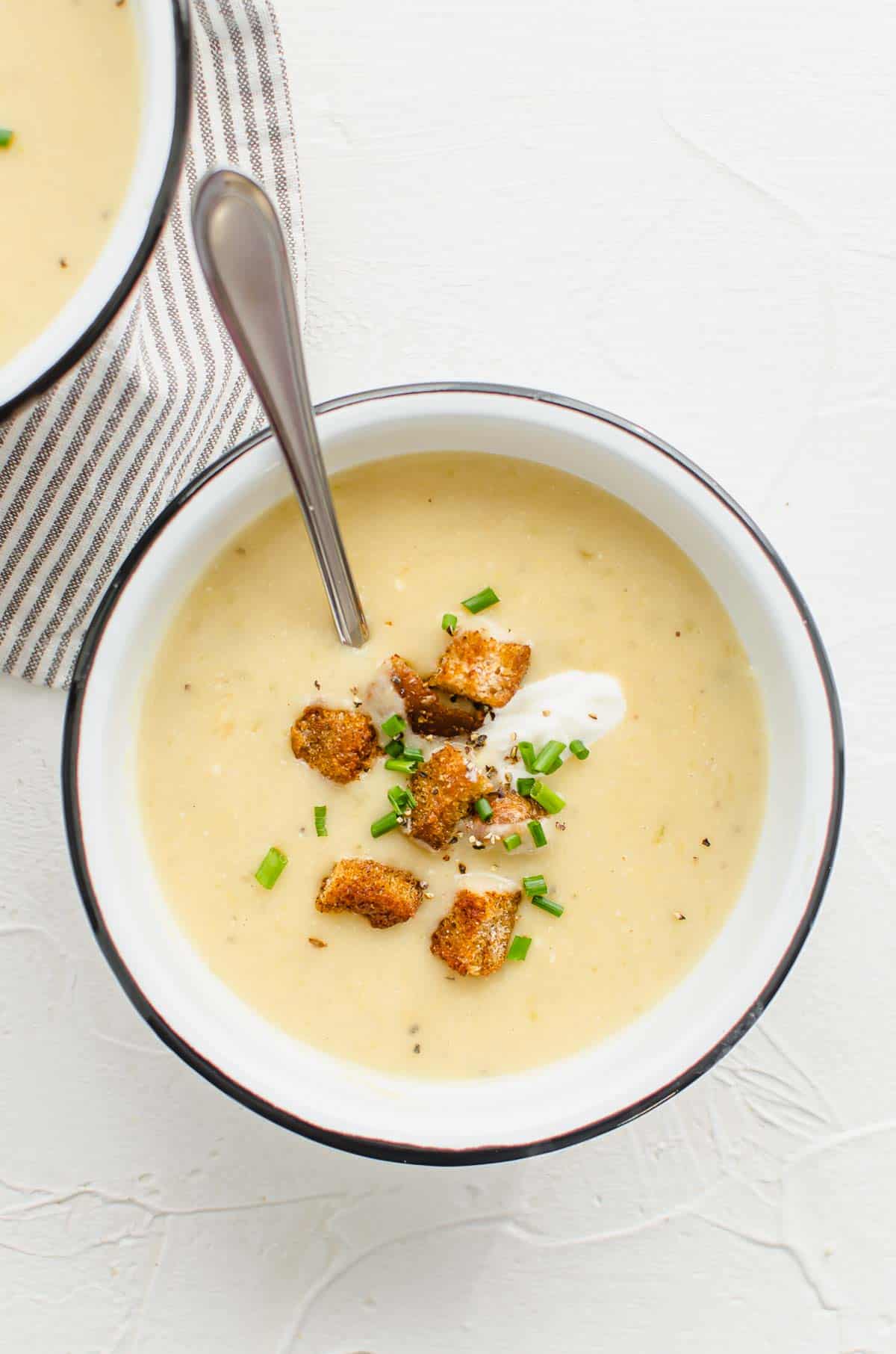 Birds eye view of vegan potato soup in a white bowl with a spoon topped with croutons, sour cream, and chives. 