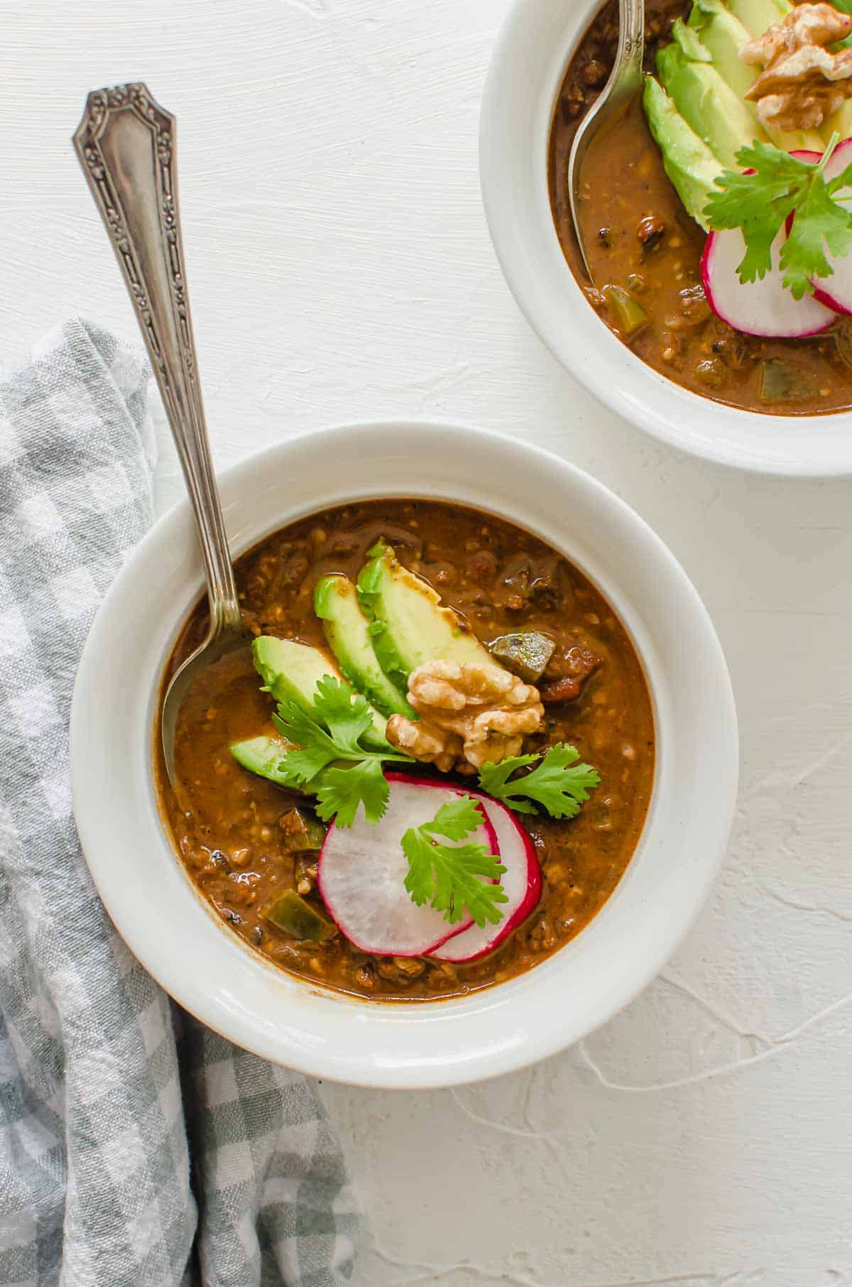 Overhead photo of a white bowl containing a no bean chili topped with avocado, radish, and cilantro. 