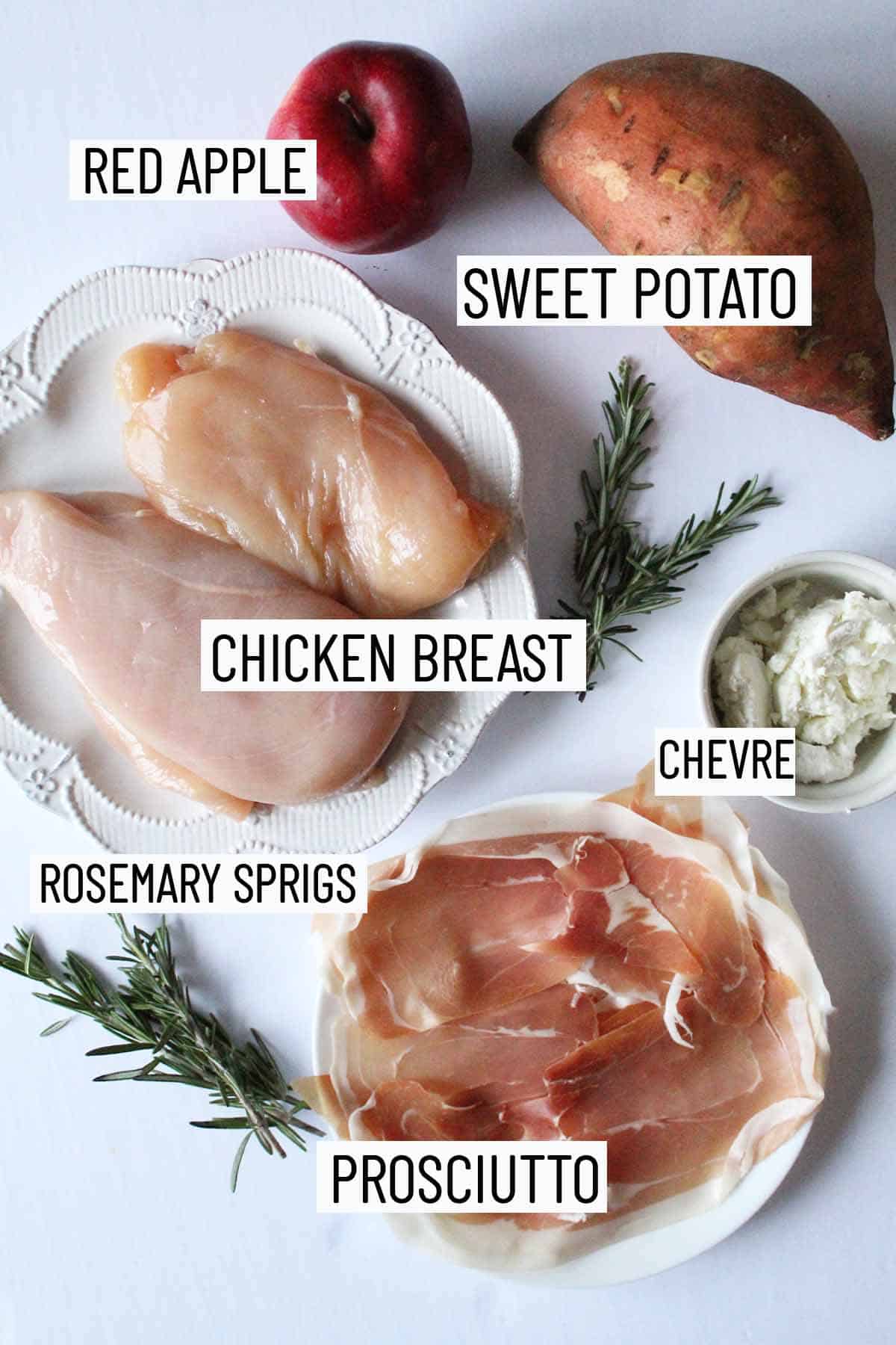 Flat lay of portioned recipe ingredients including chicken breast, sweet potato, apple, chevre, rosemary, and prosciutto. 