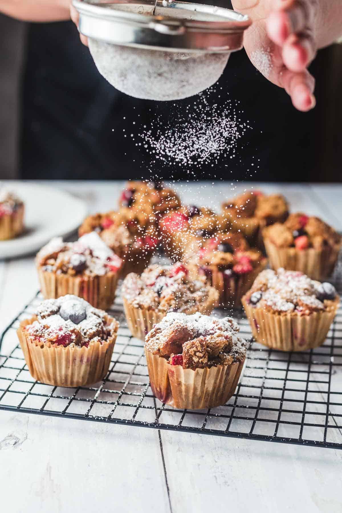 Bread pudding muffins on a cooling rack with powdered sugar being dusted on.