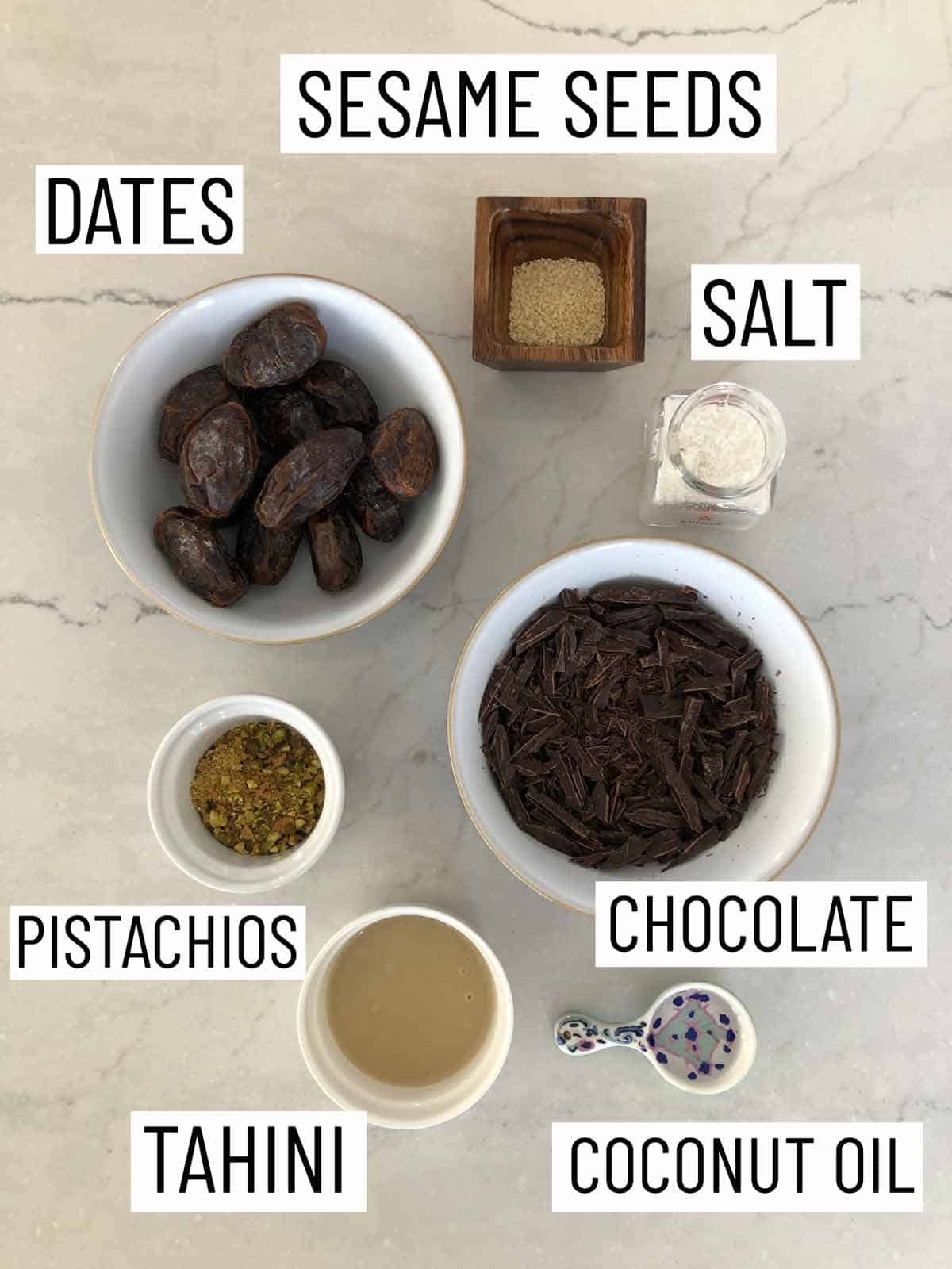 Overhead image of ingredients: dates, sesame seeds, salt, chocolate, coconut oil, tahini, and pistachios.