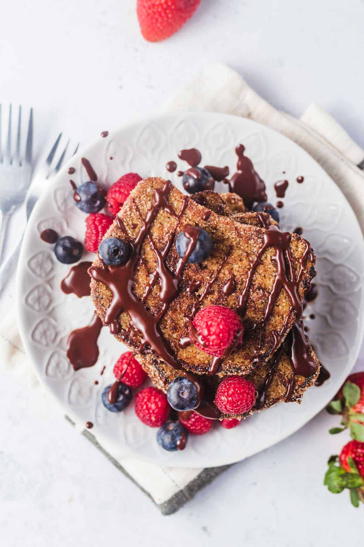 Birds eye view of churro French toast stacked on a plate topped with berries and drizzled with chocolate sauce. 