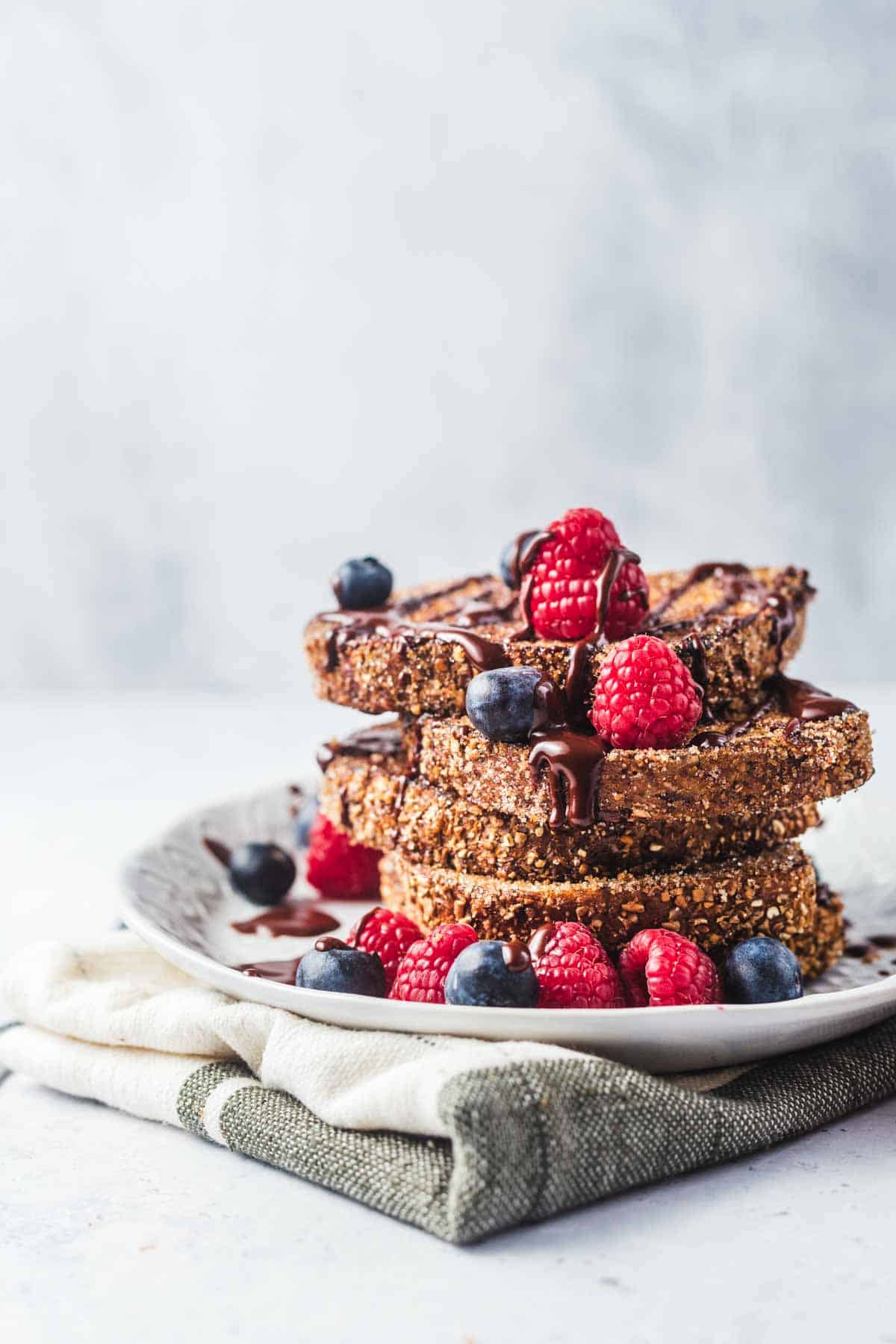 Churro french toast stacked on a plate and topped with berries and chocolate.