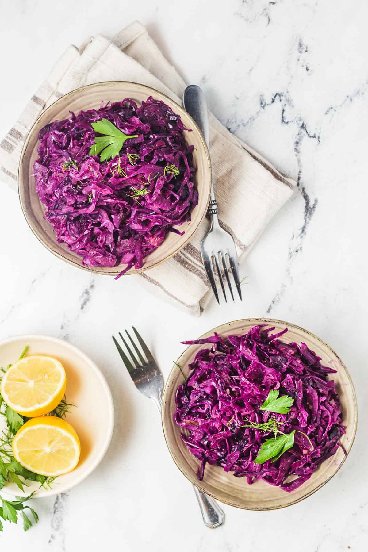 Birds eye view of two servings of instant pot cabbage in brown coloured bowls and garnished with parsley with a halved lemon on the side.
