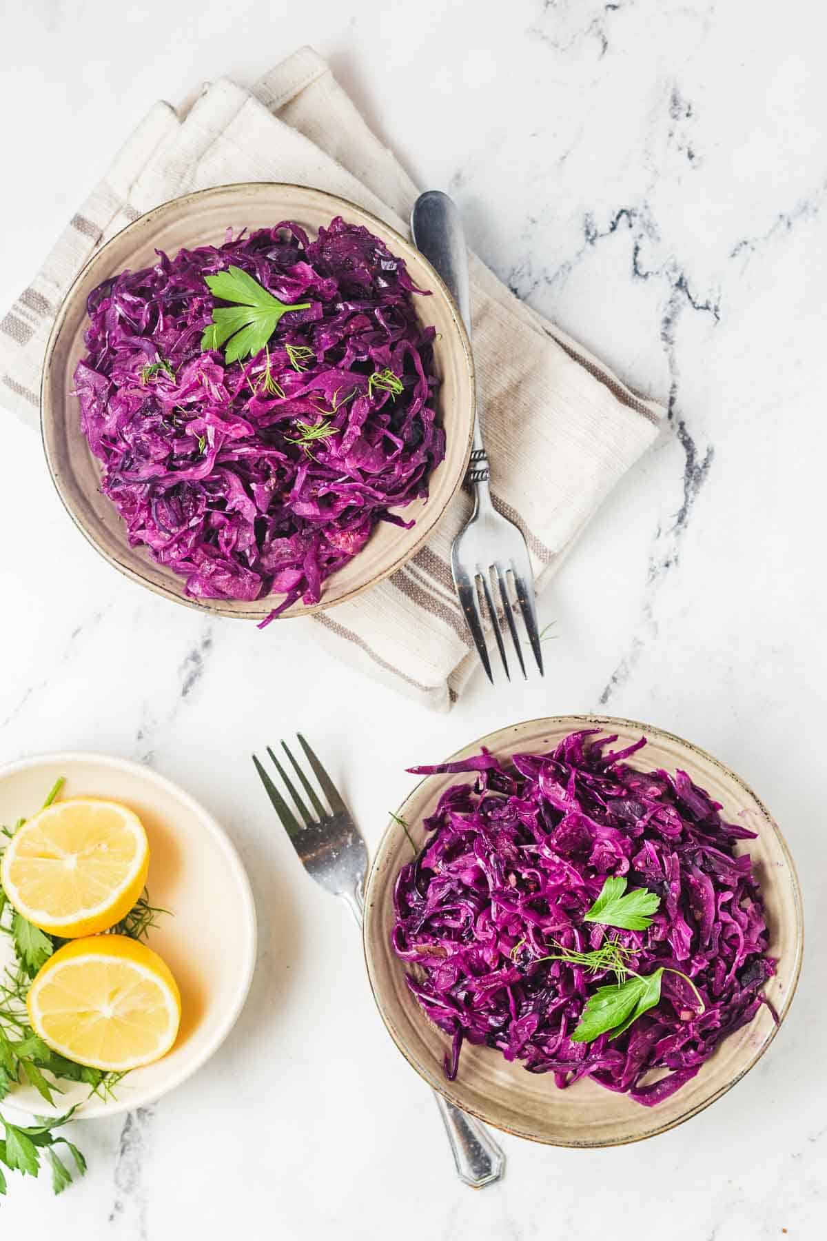 Birds eye view of two servings of instant pot cabbage in brown coloured bowls and garnished with parsley with a halved lemon on the side. 