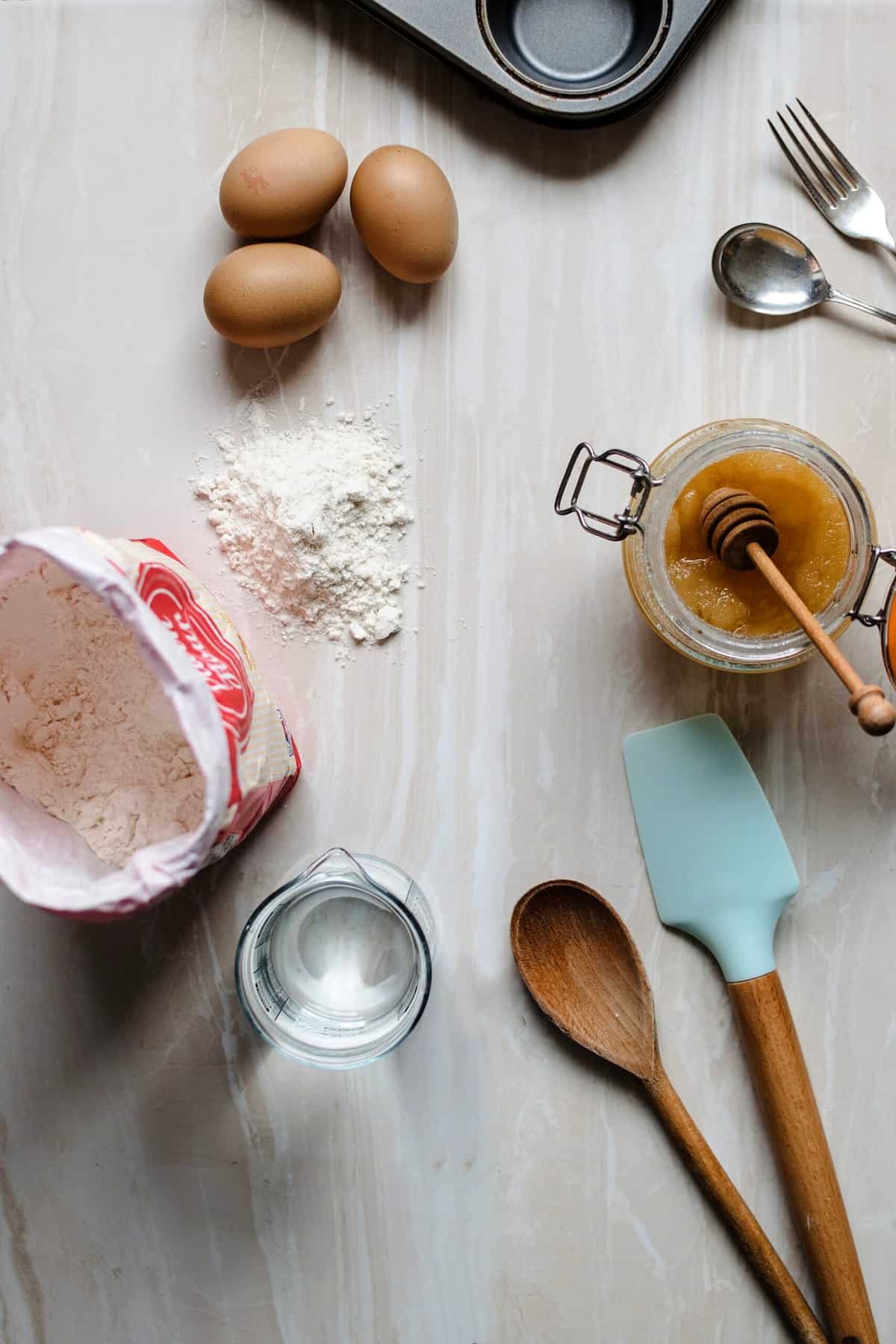 Birds eye view of baking ingredients including eggs, flour, and wooden spoons and spatulas.