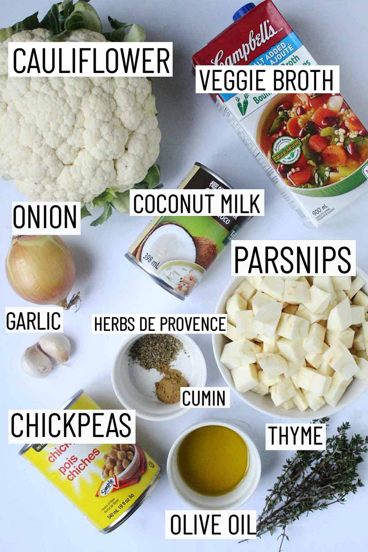 Flat lay image of recipe ingredients including thyme, olive oil, chickpeas, spices, cauliflower, parsnips, coconut milk, garlic, onion, and broth. 