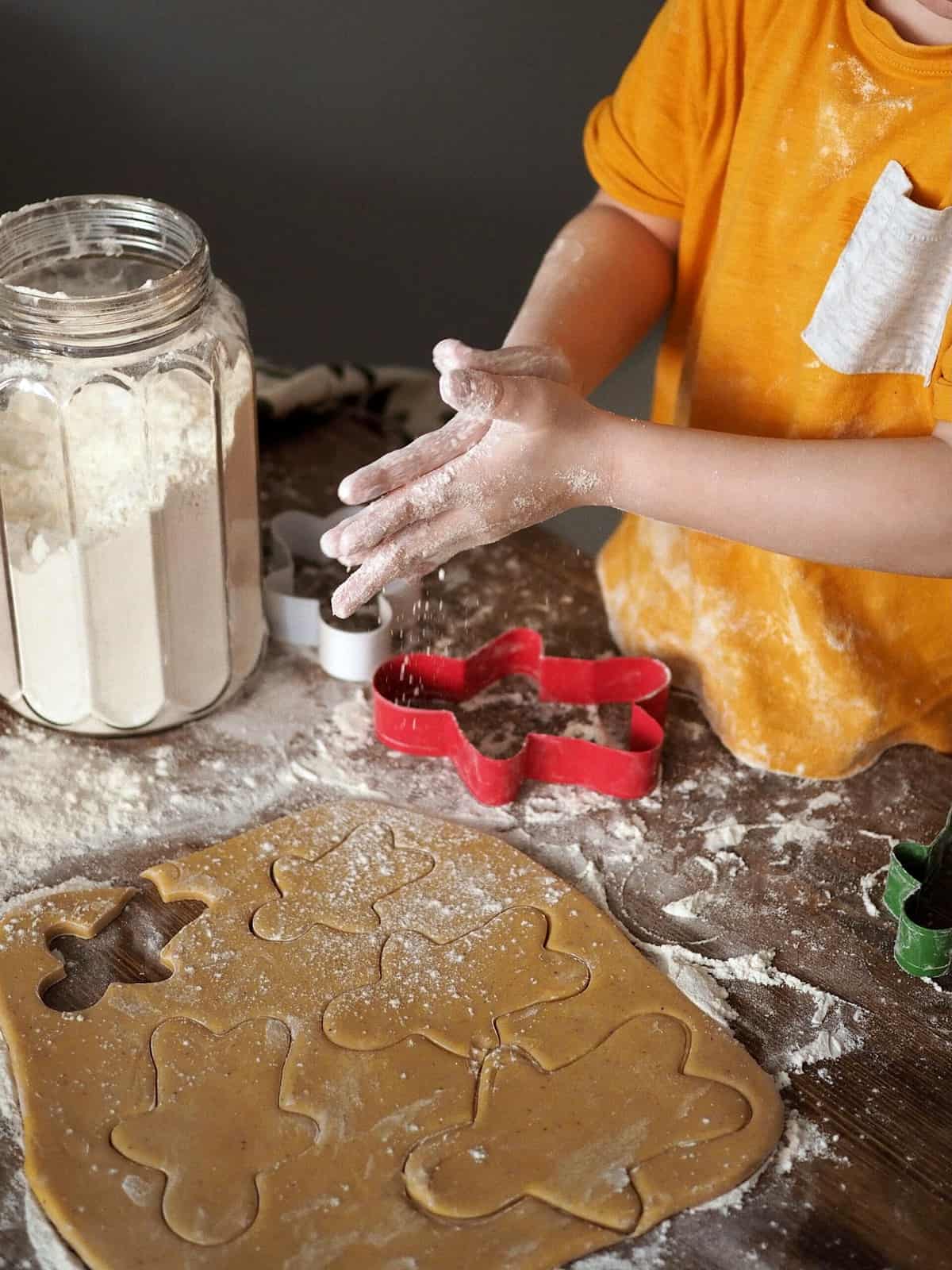 A small child making gingerbread cookies and dusting hand with flour.