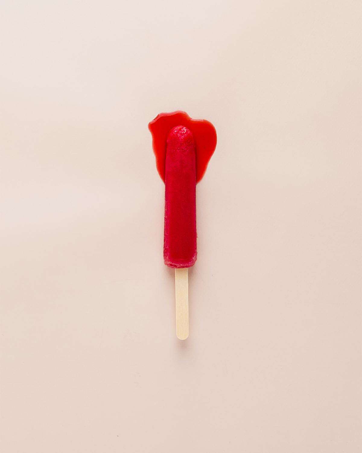 A red popsicle melting against a pink wall. 