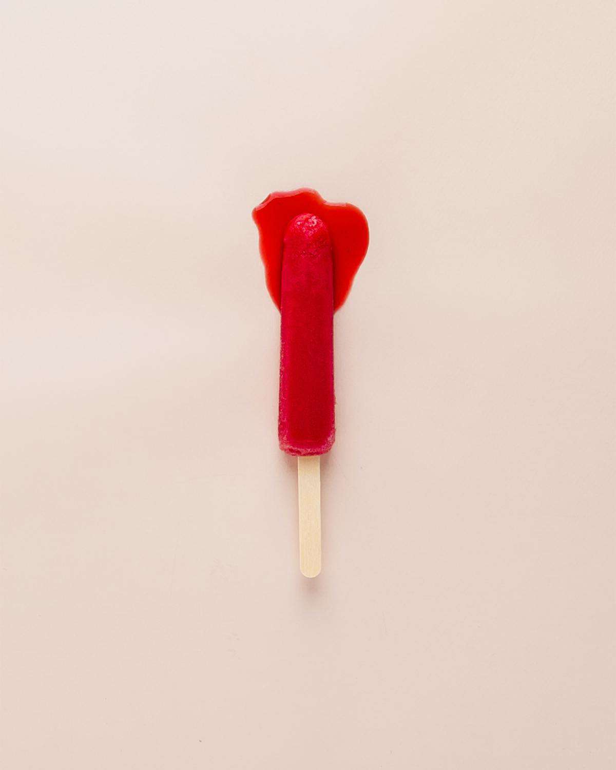 A red popsicle melting against a pink wall.