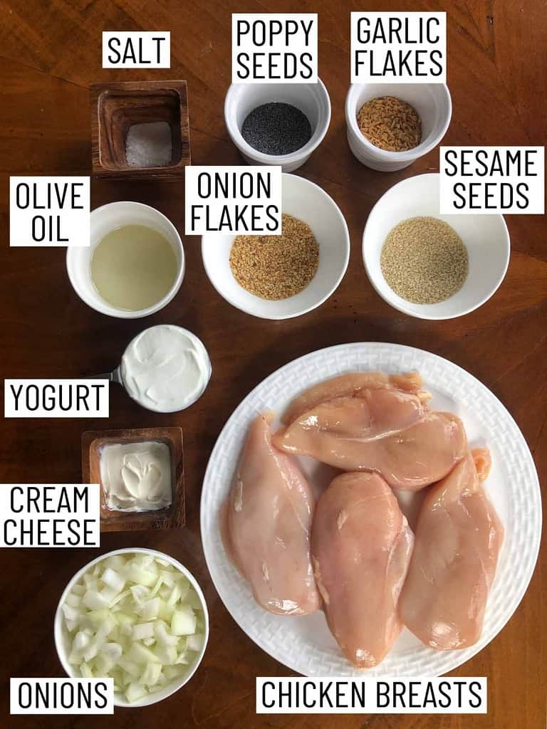 Overhead image of ingredients for everything bagel chicken breasts: chicken breasts, onions, cream cheese, yogurt, olive oil, salt, poppy seeds, garlic flakes, onion flakes, sesame seeds.