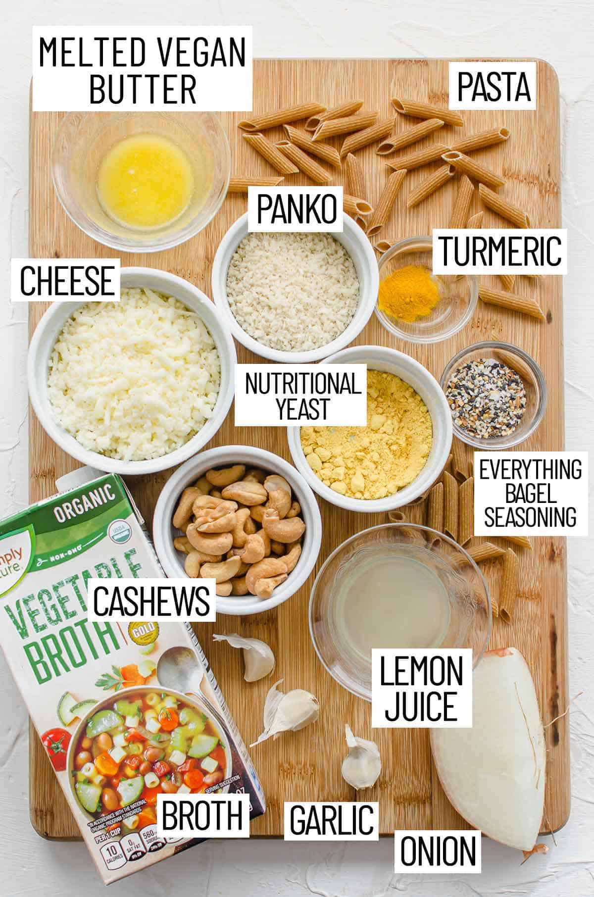 Overhead photo of ingredients for everything bagel mac and cheese including broth, garlic onion, lemon juice, everything bagel seasoning, nutritional yeast, cheese, panko, turmeric, pasta, and melted butter.