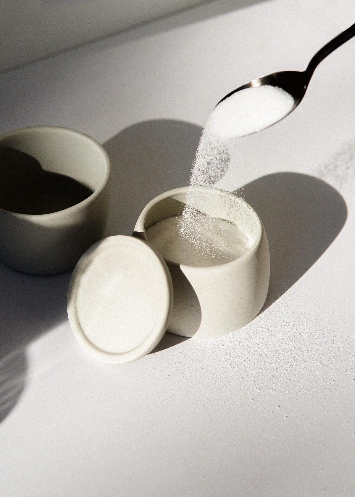 A spoon pouring sugar into a ceramic container. 
