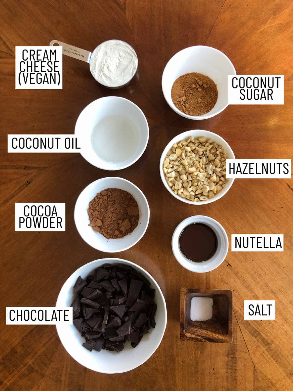 Overhead image of ingredients for no bake nutella cheesecake cups: cream cheese, coconut oil, cocoa powder, chocolate, salt, nutella, hazelnuts, coconut sugar.