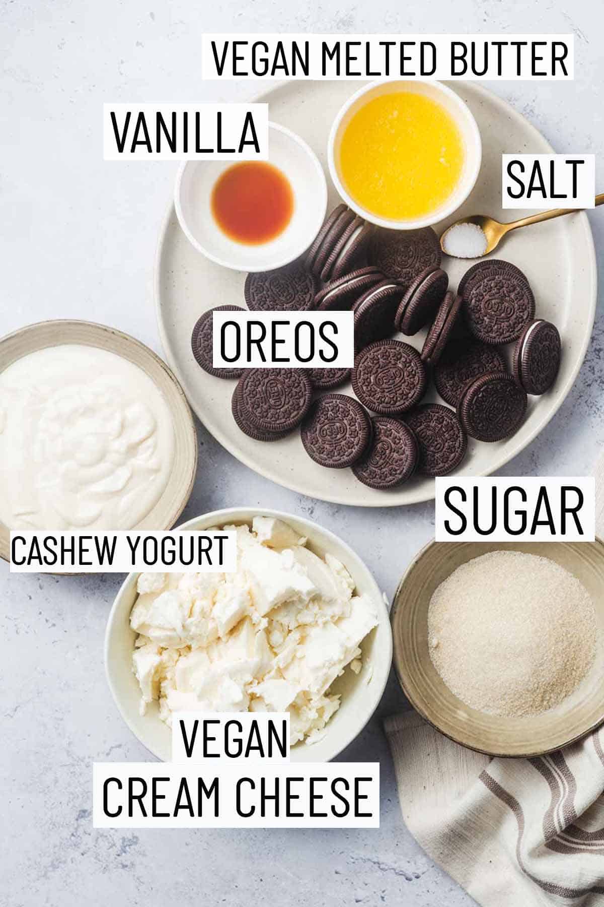 Flat lay image of recipe ingredients including sugar, cream cheese, cashew yogurt, Oreos, salt, melted butter, and maple syrup.