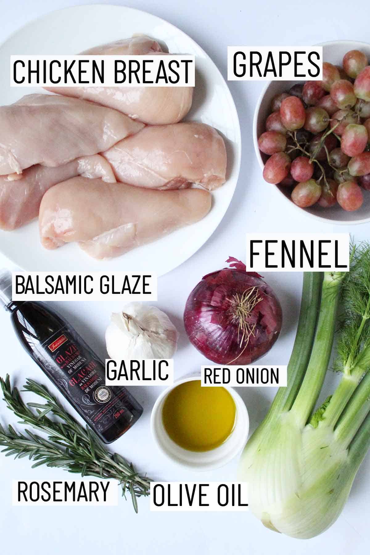 Flay lay image of recipe ingredients including chicken breast, grapes, fennel, balsamic glaze, garlic, red onion, olive oil, and rosemary. 