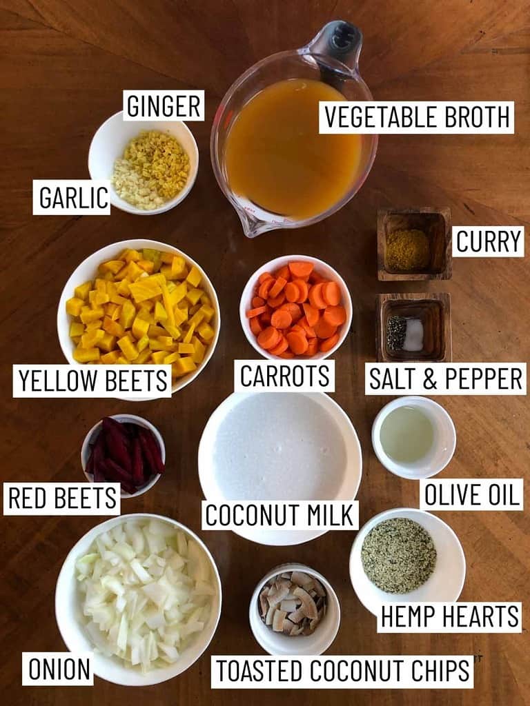 Overhead photo of ingredients for a vegan curry including vegetable broth, curry, salt and pepper, olive oil, hemp hearts, toasted coconut chips, onion, red beets, yellow beets, coconut milk, carrots, garlic, and ginger.