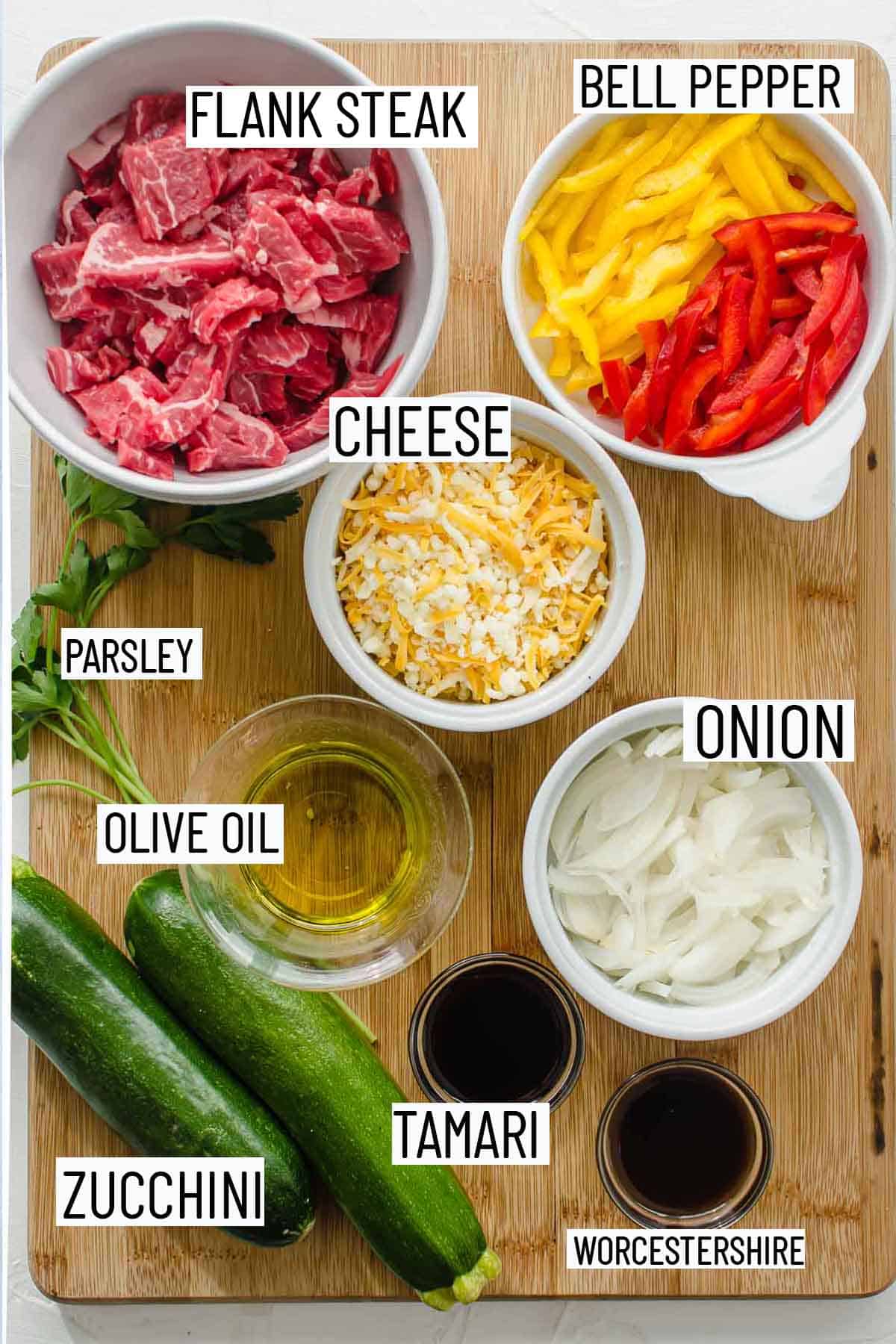 Flat lay of portioned ingredients for zucchini boats including steak, bell pepper, cheese, parsley, onion, olive oil, zucchini, tamari and worestershire sauce.