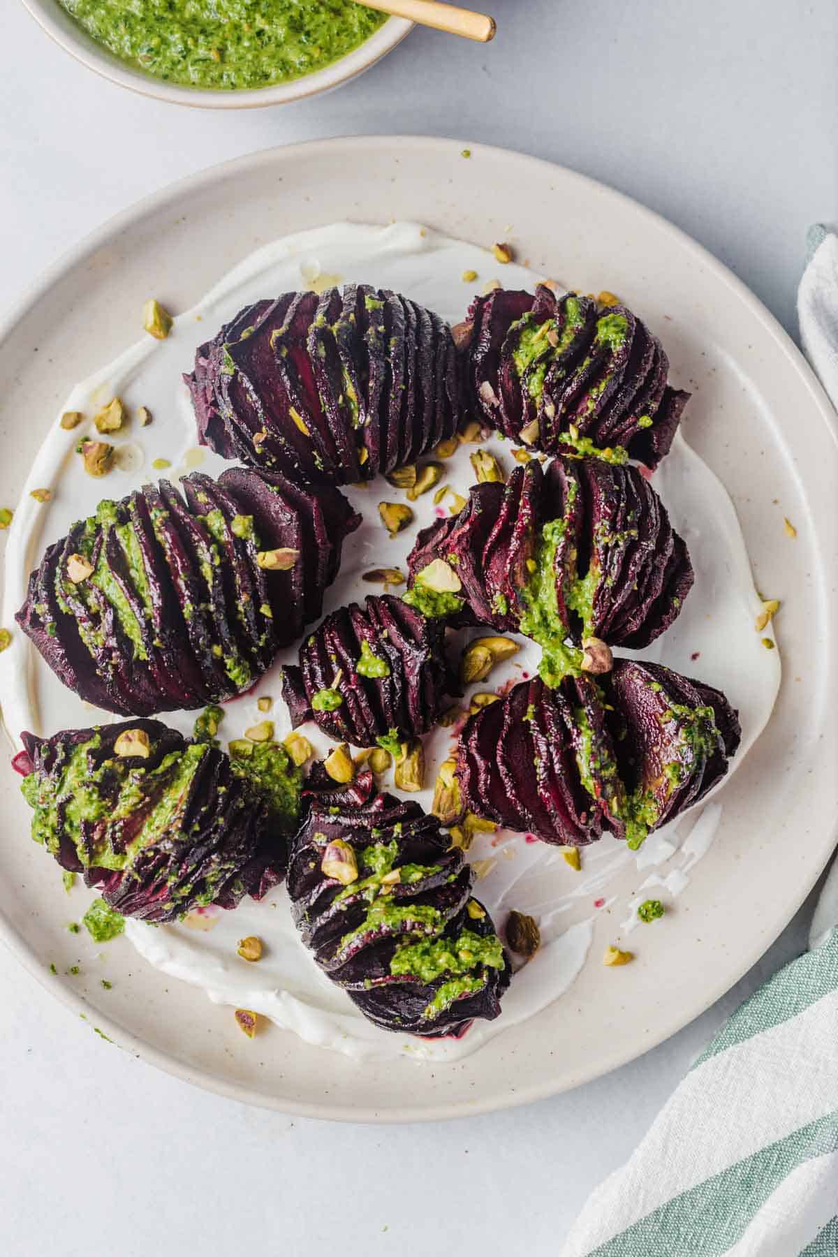 Birds eye view close up of hasselback beets on a white plate drizzled with pistachio pesto. 