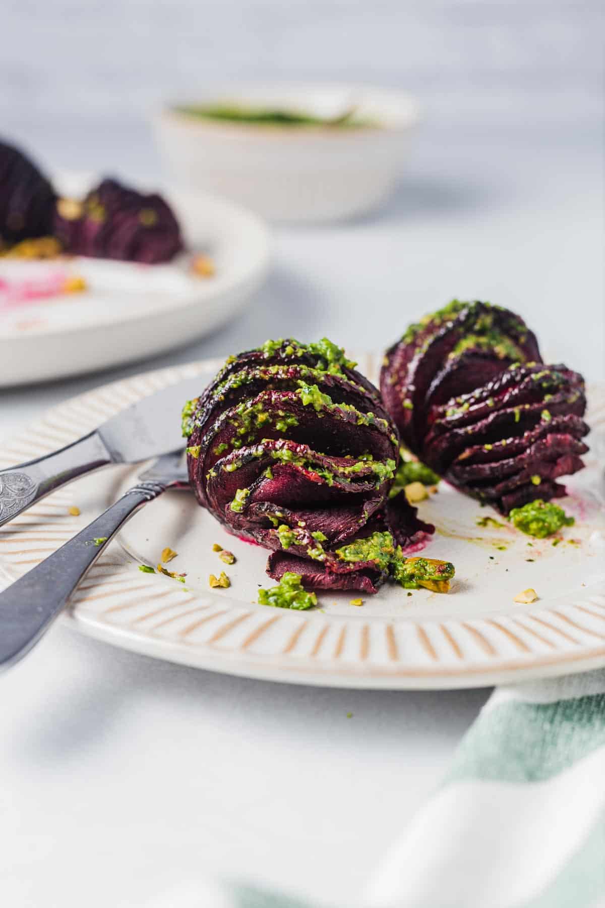Close of up two hasselback beets with pistachio pesto on a white plate. 
