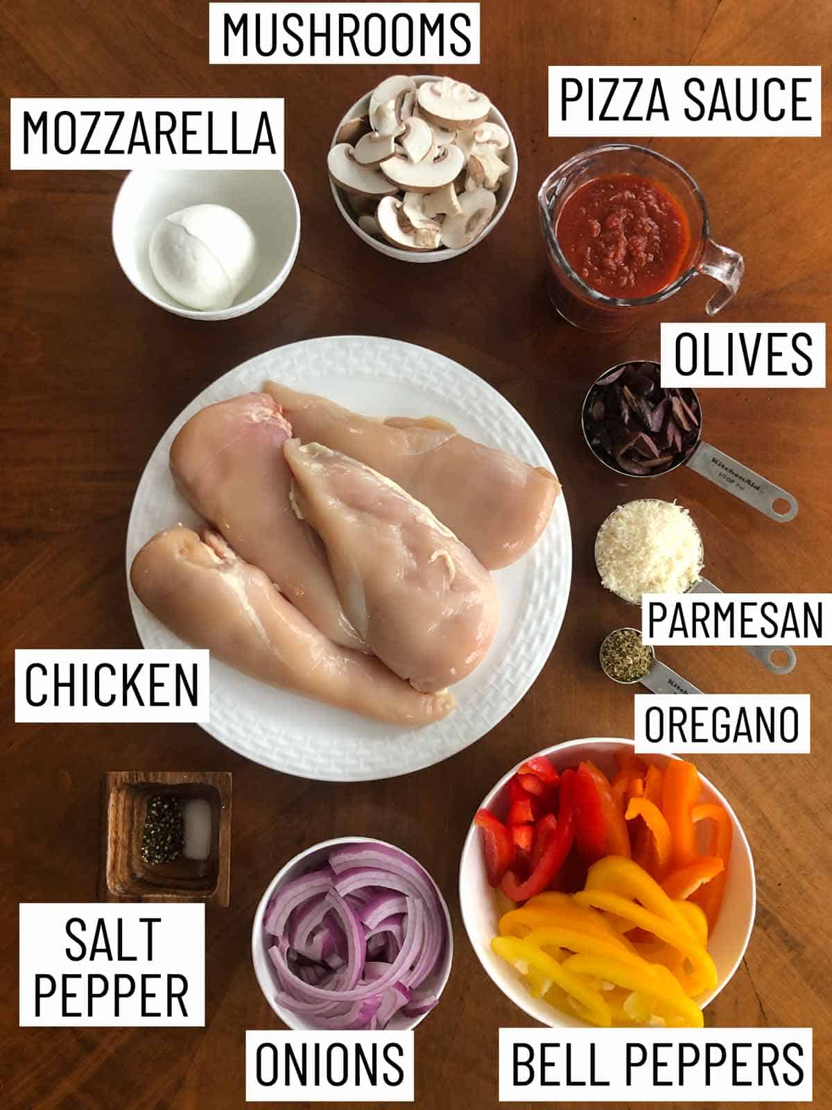 Overhead image of ingredients: mozzarella, mushrooms, pizza sauce, olives, parmesan, oregano, bell peppers, onions, salt and pepper, chicken.