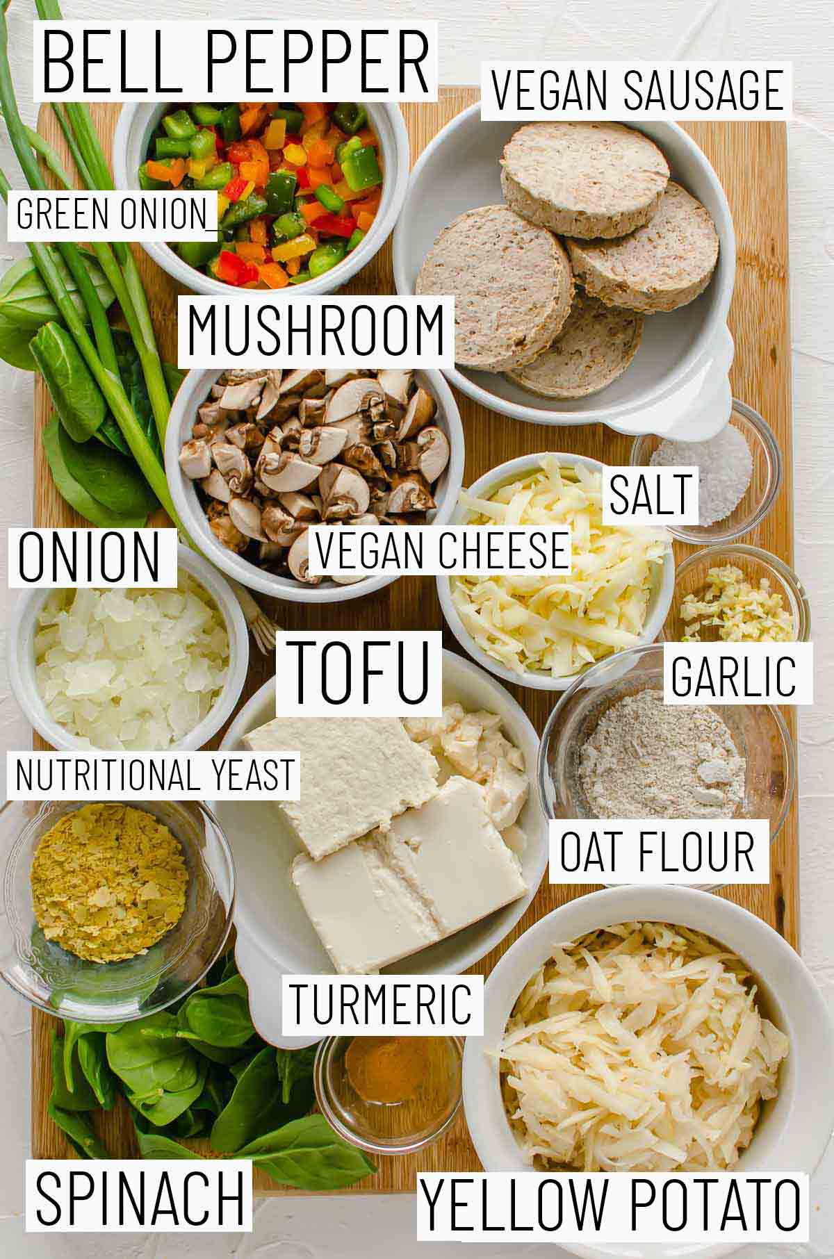 Flay lay image of portioned ingredients for the vegan breakfast casserole recipe including bell pepper, vegan sausage, green onion, mushroom, salt, vegan cheese, garlic, onion, tofu,  oat flour, nutritional yeast, turmeric, potato, and spinach. 