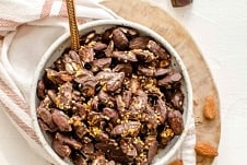 Chocolate covered almonds in a bowl on top of a serving board.