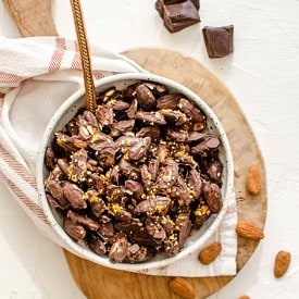 Chocolate covered almonds in a bowl on top of a serving board.