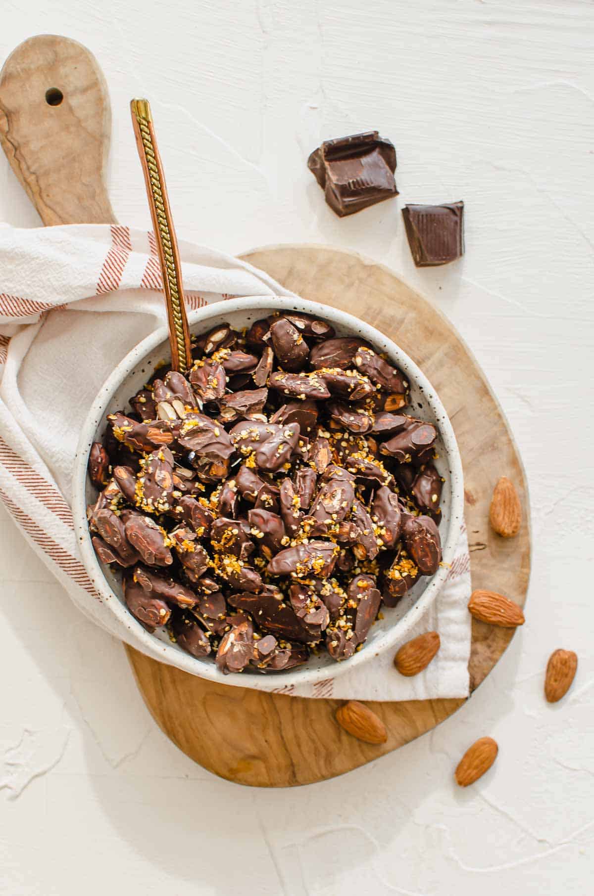 Chocolate covered almonds in a bowl on top of a serving board.