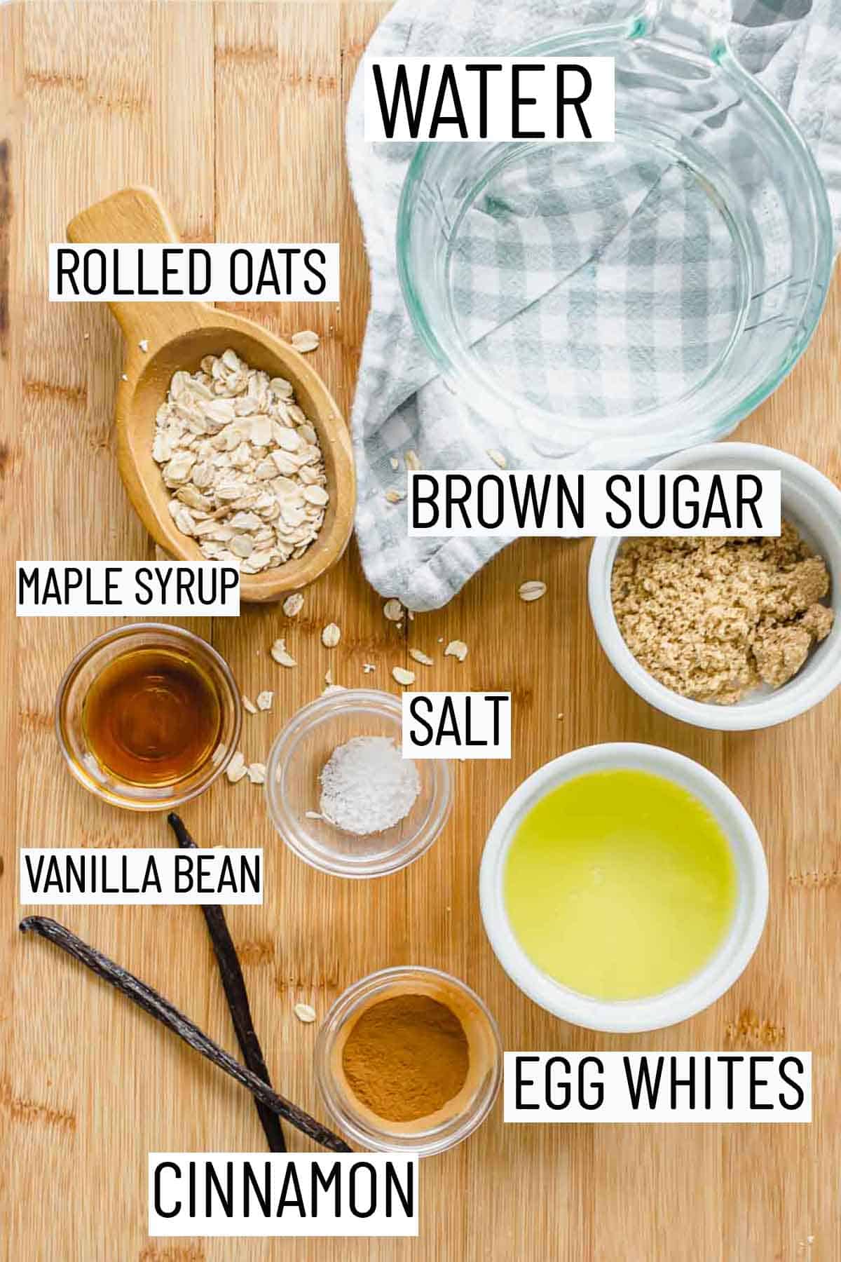 Flat lay image of portioned recipe ingredients including water, rolled oats, brown sugar, maple syrup, salt, vanilla bean, egg whites, and cinnamon. 
