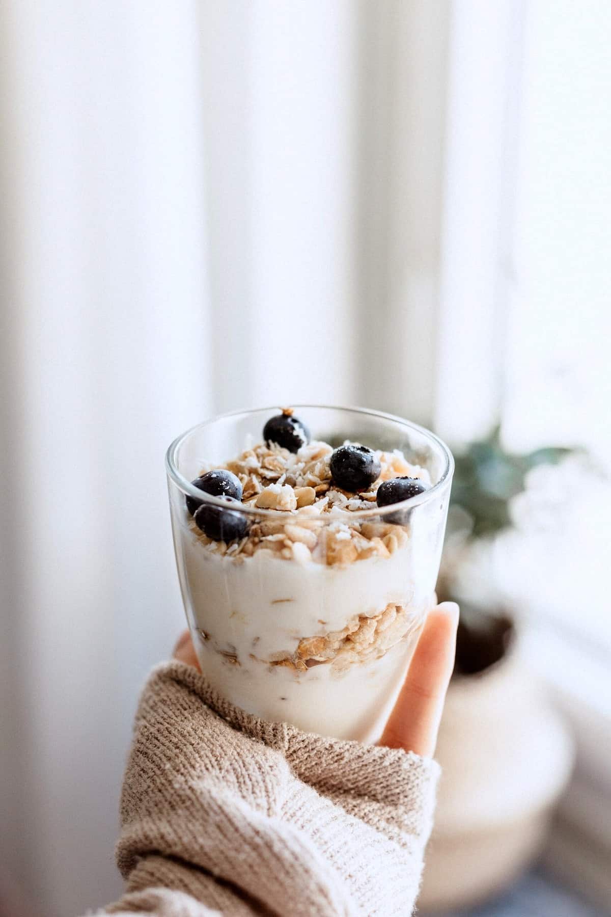 A hand holding up a breakfast parfait with blueberries and granola. 