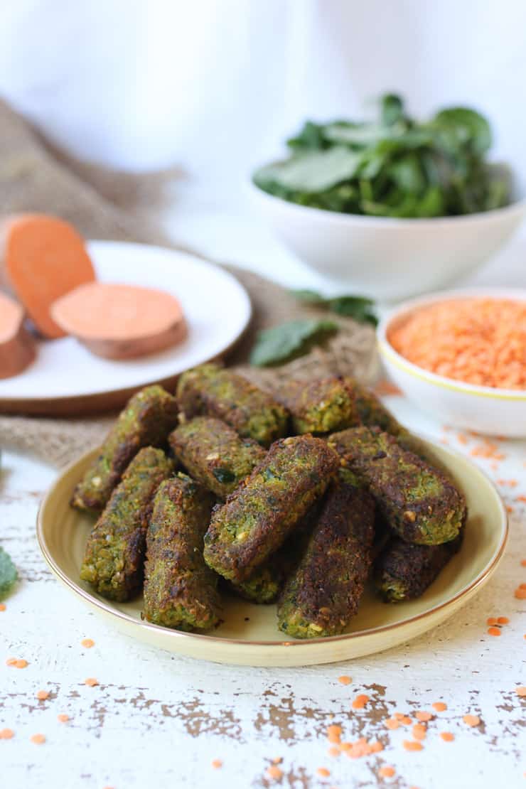Several sweet potato fritters on a yellow plate with sweet potato and kale in the background.