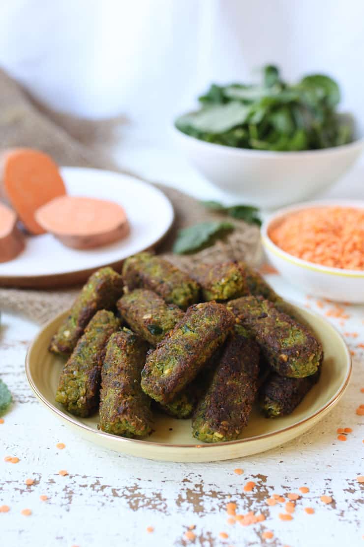 Several sweet potato fritters on a yellow plate with sweet potato and kale in the background. 