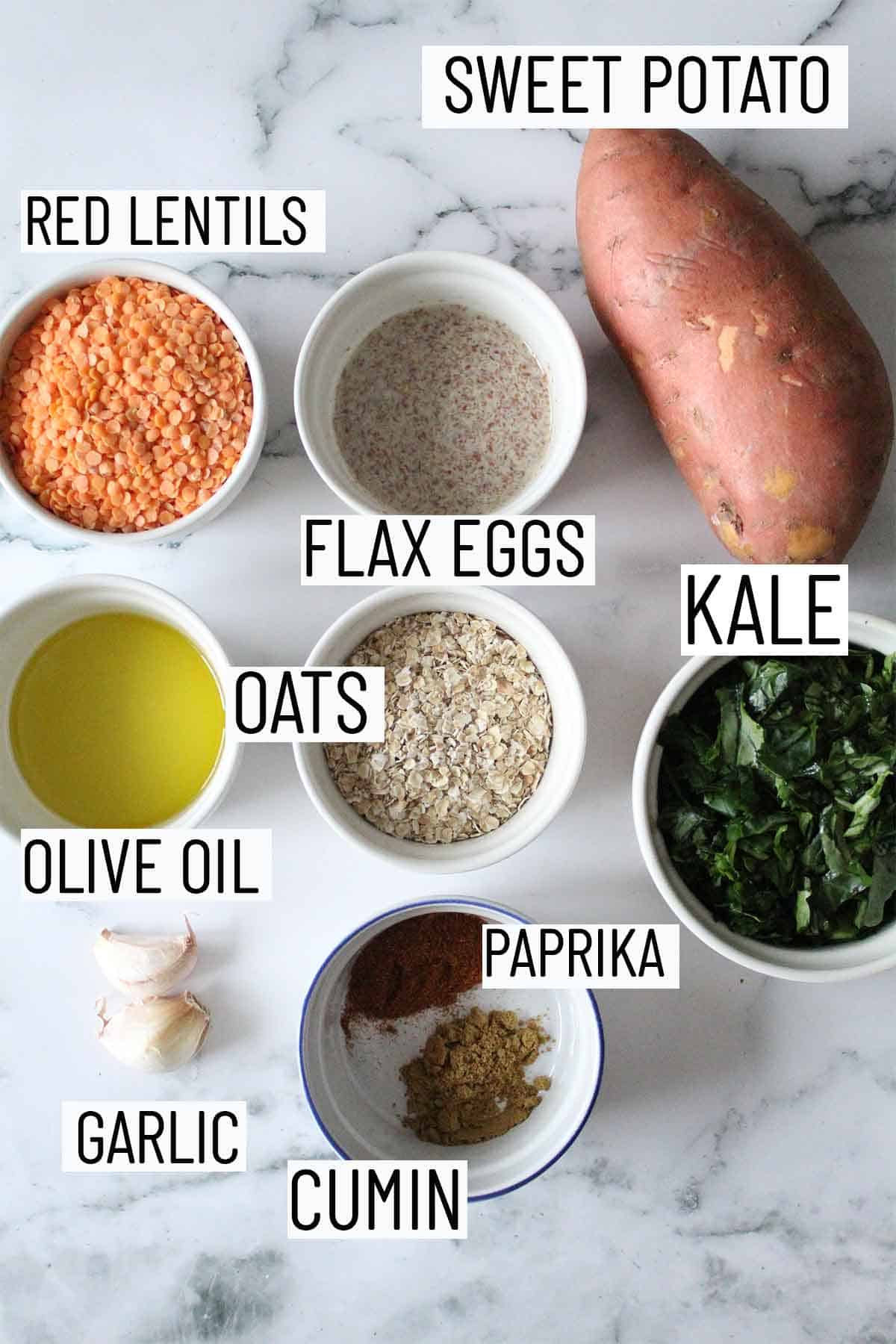 Flat lay image of portioned ingredients for recipe including sweet potato, kale, cumin, paprika, olive oil, garlic, oats, flax egg, and red lentils. 