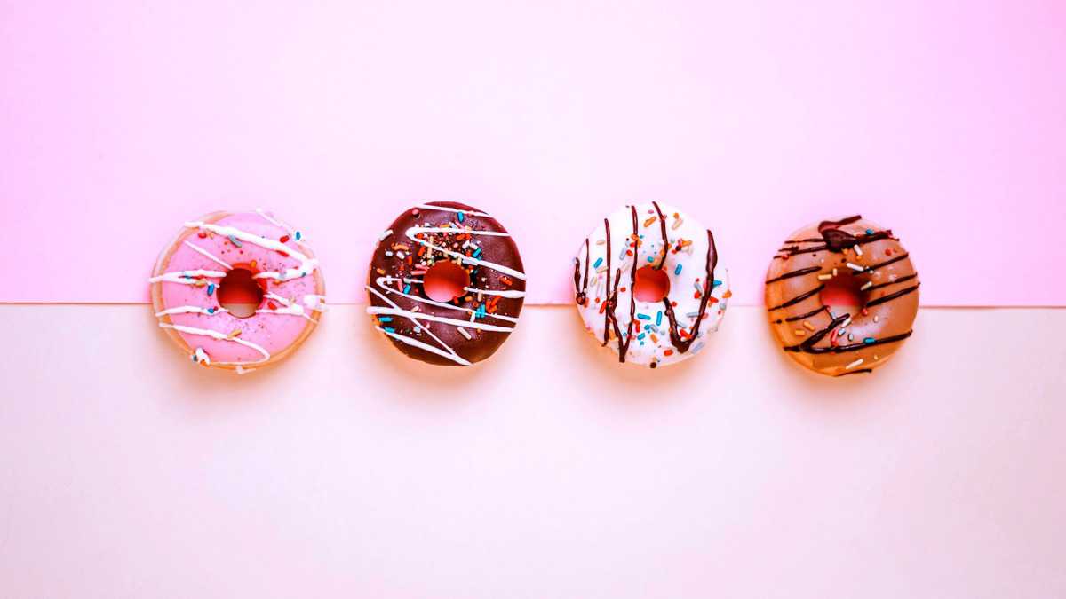 Four donuts in a line side by side and drizzled with icing and sprinkles.