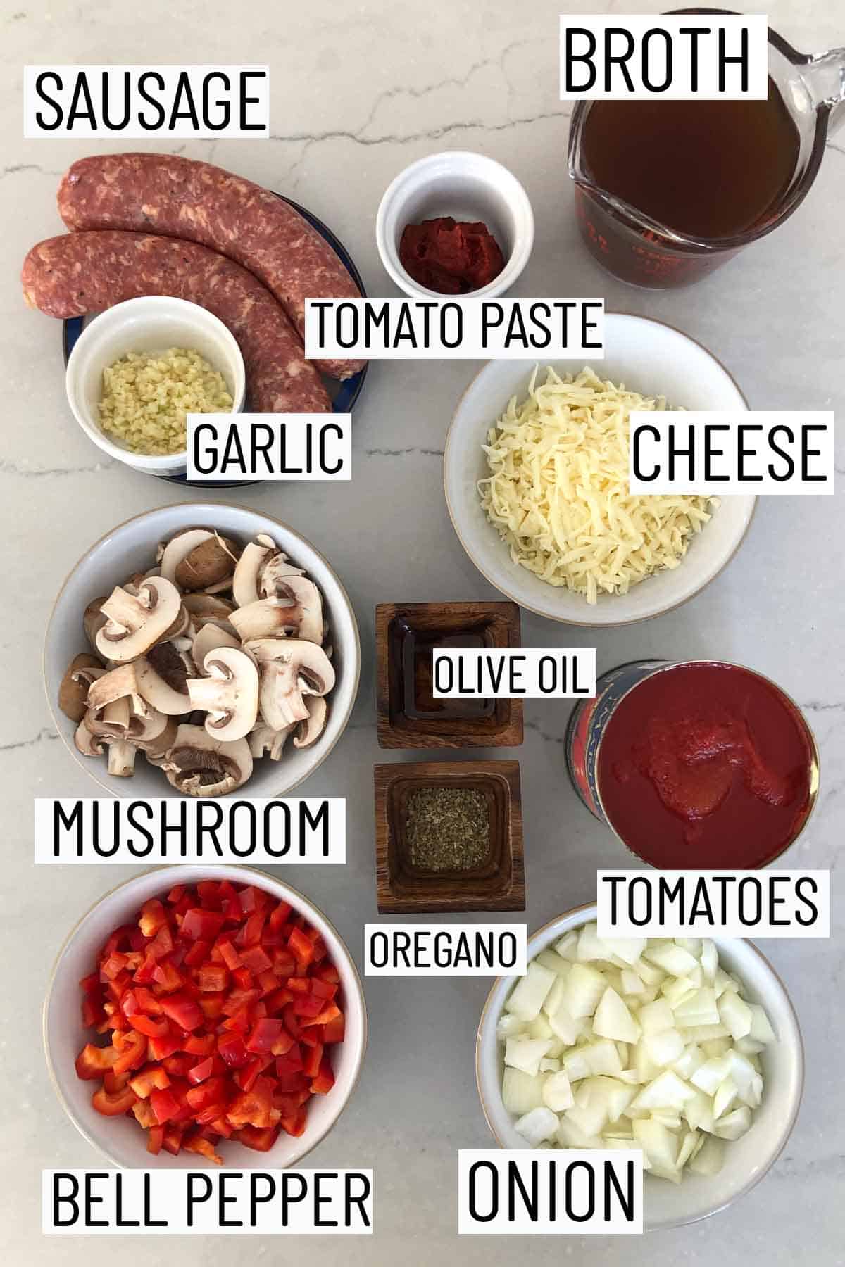 Flat lay image of portioned recipe ingredients including broth, tomato paste, sausage, garlic, cheese, olive oil, oregano, mushroom, bell pepper, onion, and tomatoes. 
