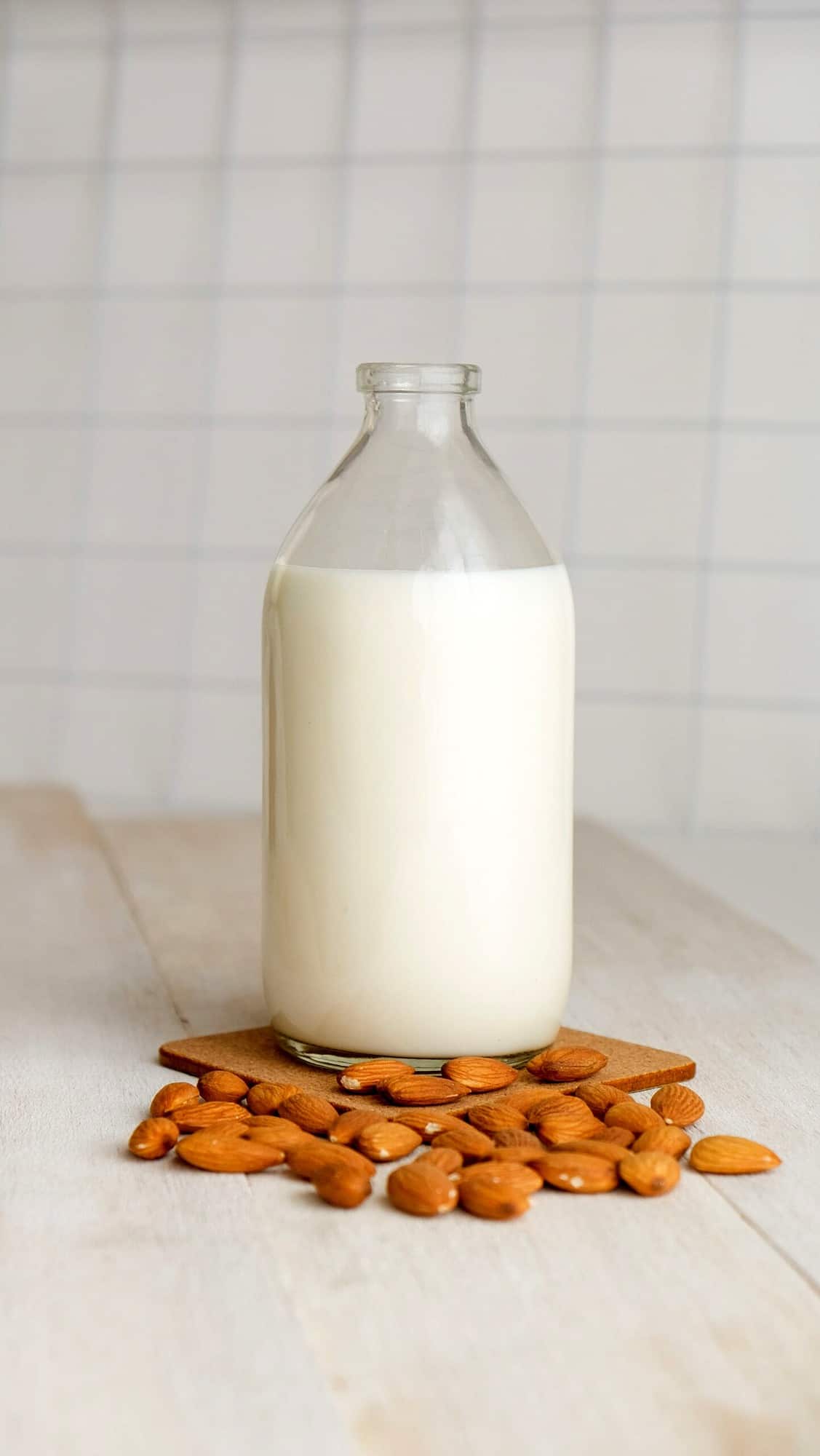 A bottle of almond milk with almonds scattered around it. 