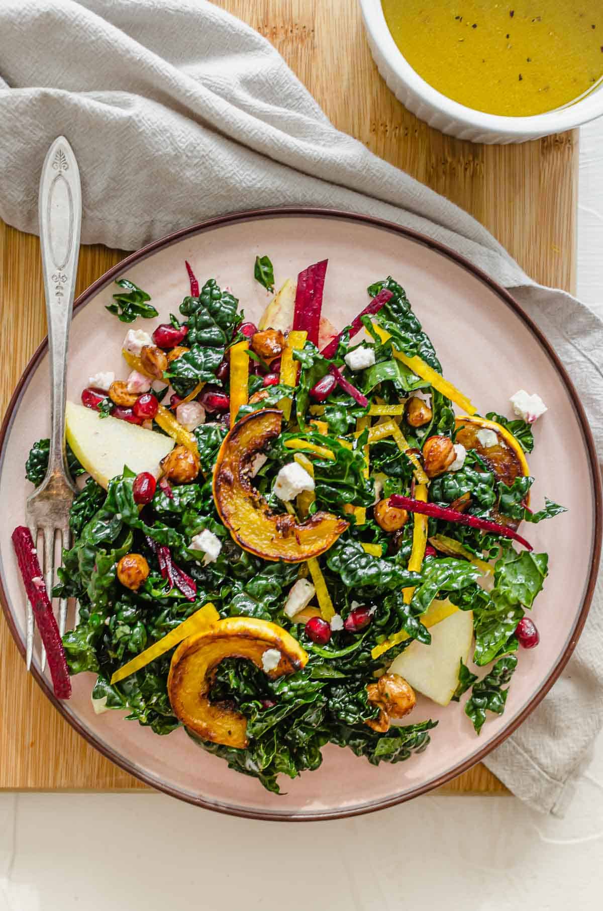 Birds eye view of sweet kale salad in a pink plate with a fork and extra dressing on the side. 