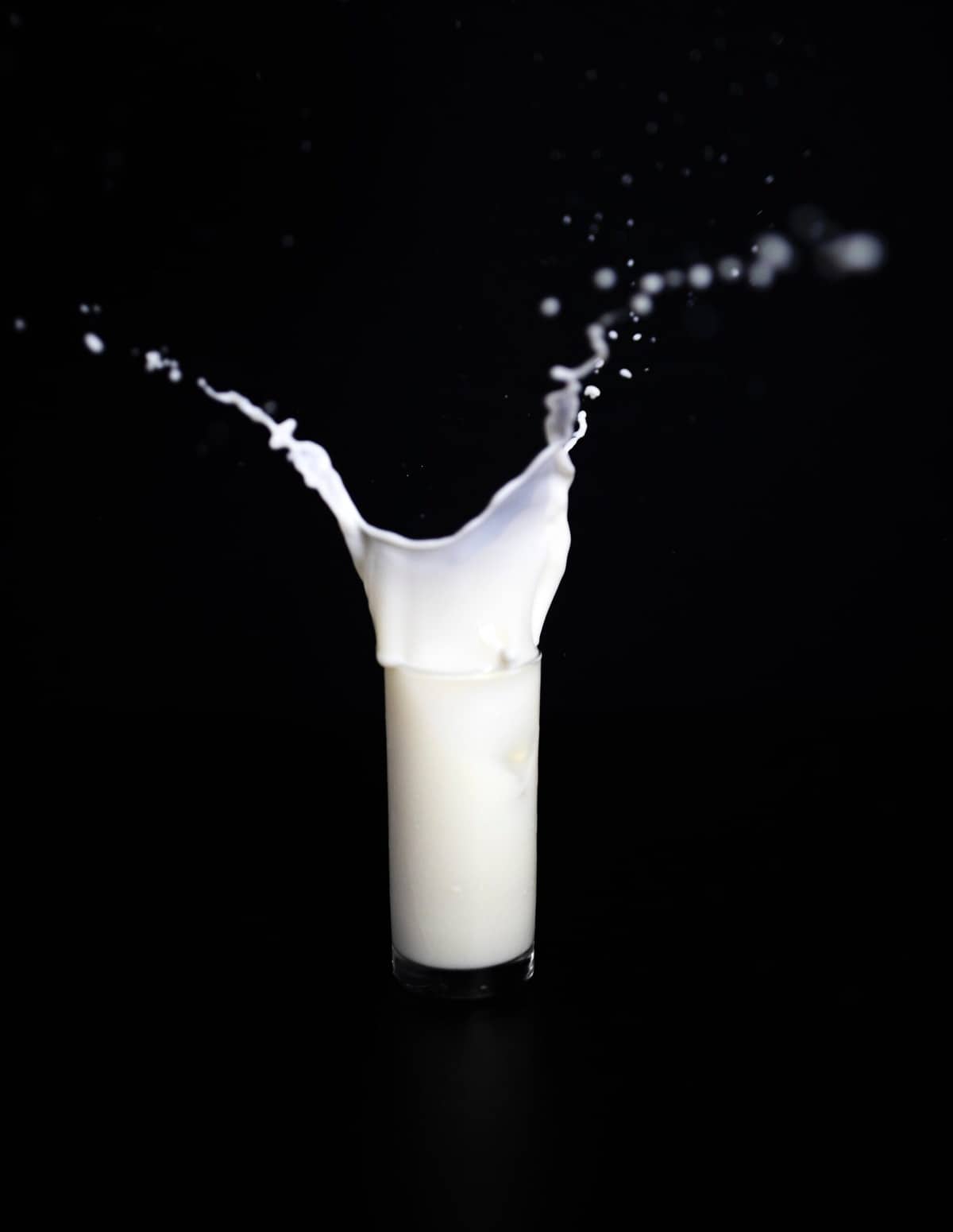A glass of milk spilling against a black background. 