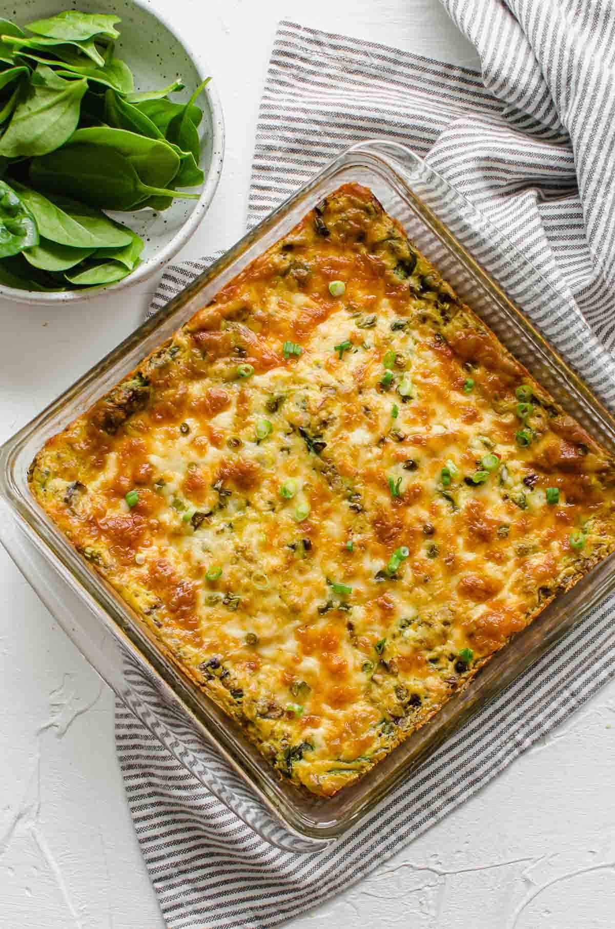 Birds eye view of vegan breakfast casserole in a casserole dish with a bowl of spinach in the background. 