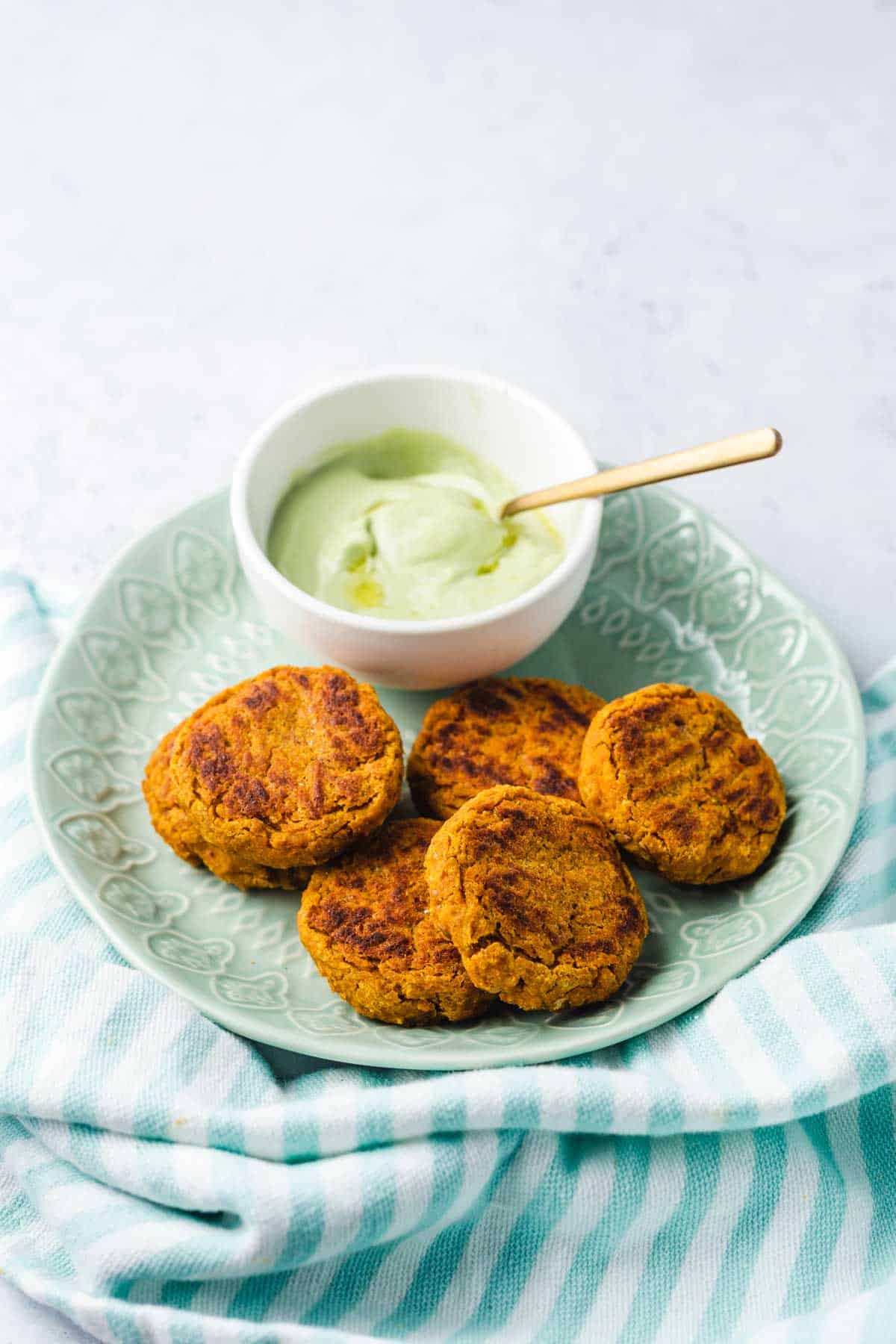 Close up image of sweet potato chickpea patties on a green plate served with avocado sauce on the side. 