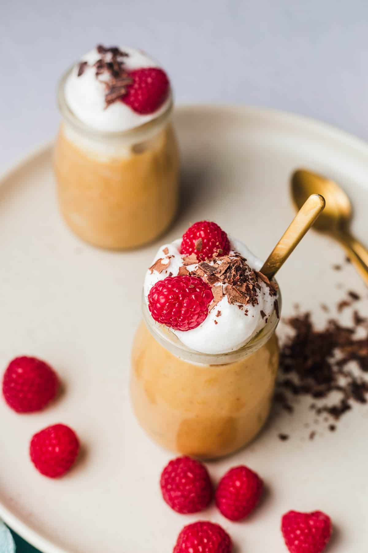 Close up of sweet potato tofu pudding in glass jars topped with raspberries, yogurt and shaved chocolate. 