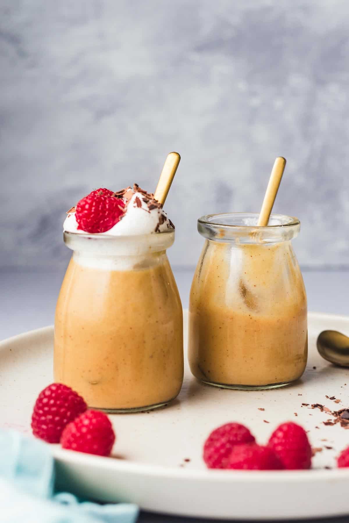 Close up of two jars of tofu pudding with one topped with yogurt, raspberries, and shaved chocolate. 